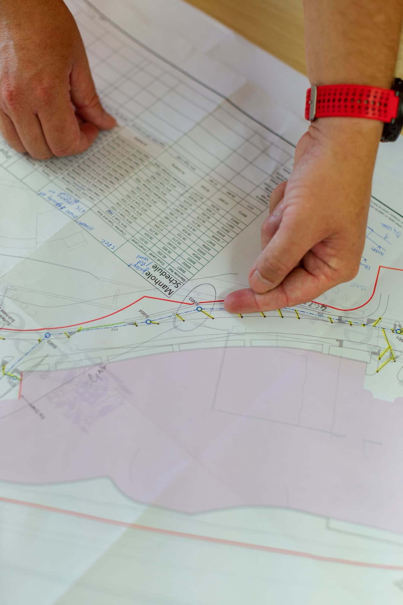 Hands working across a construction drawing and schedule